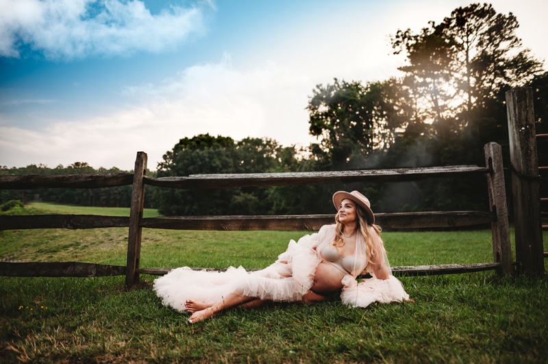 Maternity Photographer, a pregnant woman lays in the grass with a feather boa around her